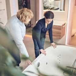 Frau Steinkühler aus Leverkusen zeigt Kundin eine Badewanne für die Teilbad Modernisierung ihres Badezimmers.