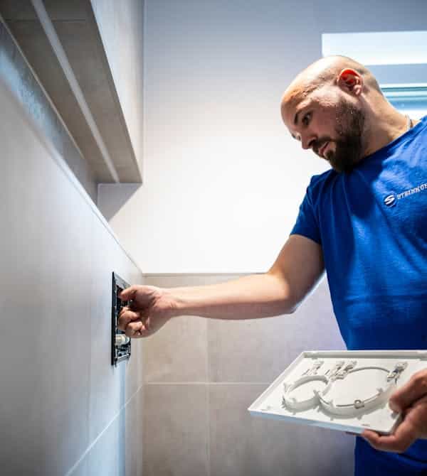 Ein Fachhandwerker führt präzise Installations- oder Wartungsarbeiten an einer modernen Haustechnikkomponente durch und hält dabei einen Bauplan zur Kontrolle bereit; die Szene steht für fachgerechte Ausführung und sorgfältige Planung – Steinkühler Wasser & Wärme GmbH & Co. KG